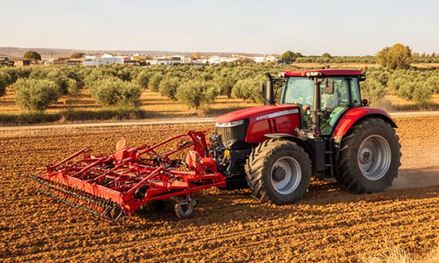 Tractor rojo con apero de tratamiento de suelo estacionado en una explotación sevillana