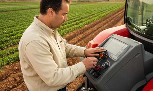 Persona revisando las especificaciones de un tractor junto a una parcela agrícola