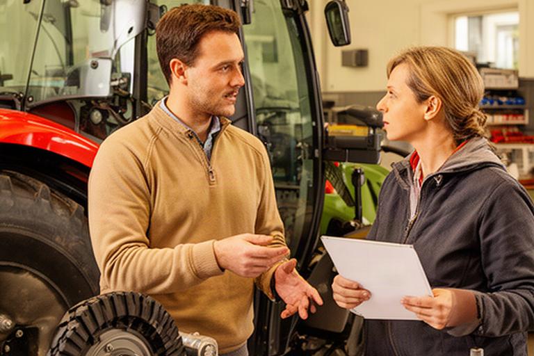 Profesional atendiendo una consulta sobre un tractor agrícola junto a una mesa de trabajo